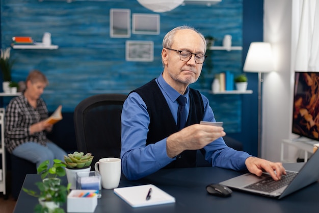 Free photo senior man reading cvv conde on credit card wearing glasses