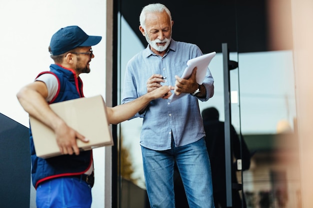 Senior man receiving home delivery while courier is pointing at place he need to sign