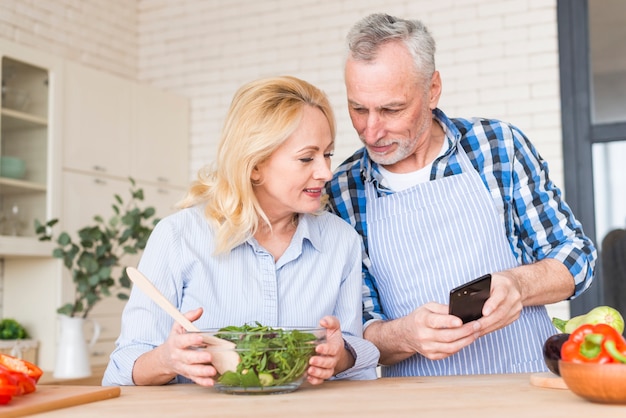 Senior man showing something to his wife on mobile phone in the kitchen