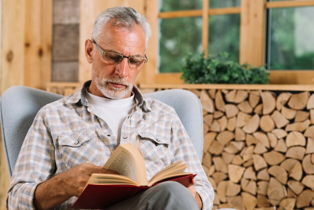 Uomo senior che si siede sul libro di lettura della poltrona