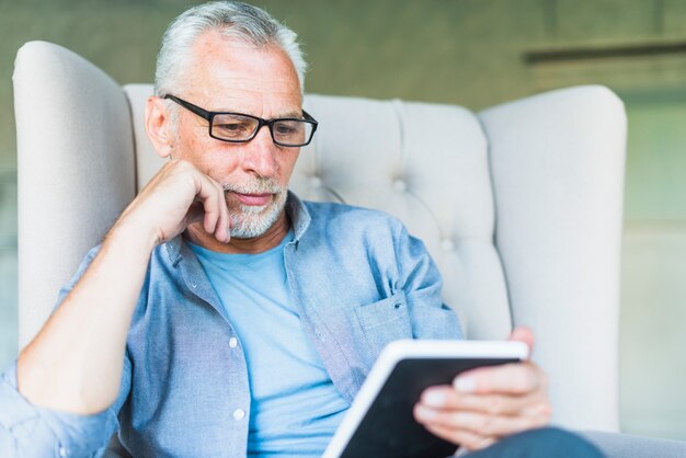Senior man sitting on armchair looking at digital tablet
