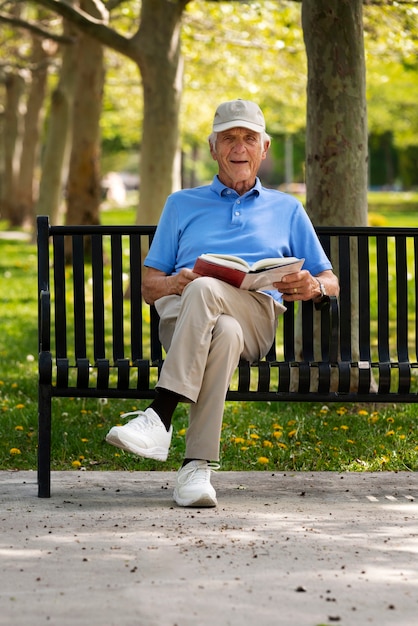 屋外のベンチに座って本を読む年配の男性