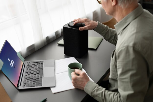 Senior man sitting at desk turning on a speaker in living room