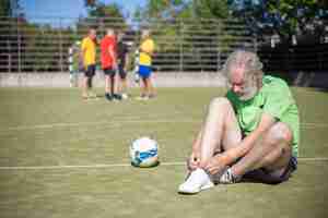 Foto gratuita senior uomo seduto sul campo lacci di legatura. uomo con la barba grigia in abiti sportivi che si prepara per l'allenamento. concetto di calcio, sport, attività ricreative