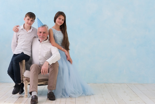 Free photo senior man sitting his grandchildren on arm chair looking at camera