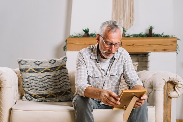 Senior man sitting in living room looking at photo frame