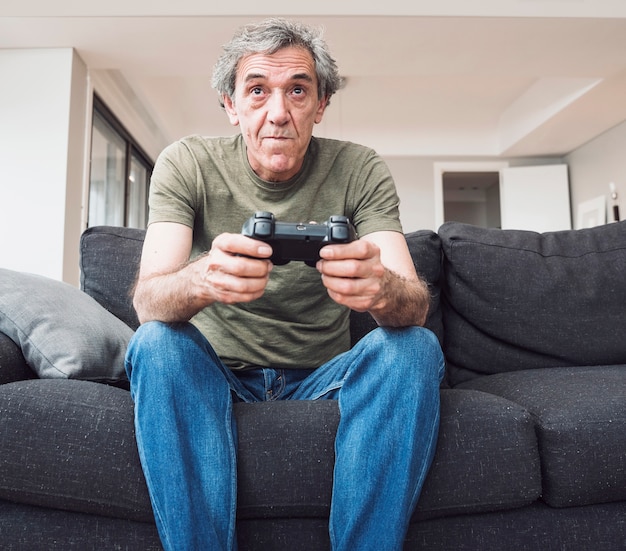 Бесплатное фото Старший человек, сидя на диване, играя в видеоигры с джойстиком