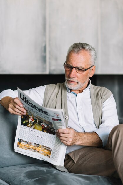 Старший мужчина, сидящий на диване, читающий газету