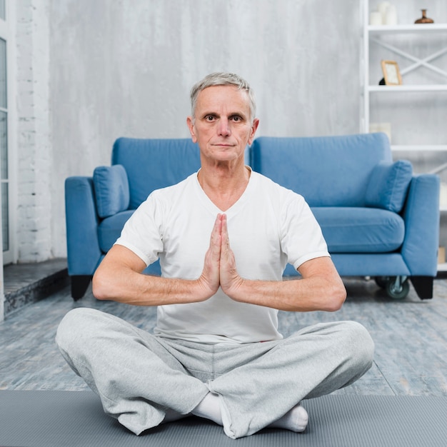 Foto gratuita uomo senior che si siede sulla stuoia di yoga che fa gesto di preghiera