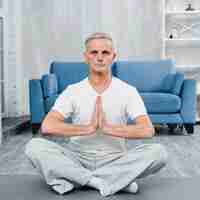 Free photo senior man sitting on yoga mat doing praying gesture