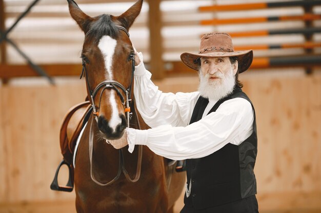 A senior man standing close to a horse outdoors in nature