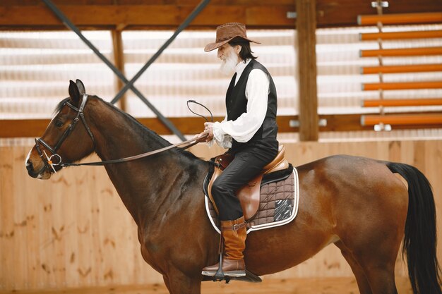 A senior man standing close to a horse outdoors in nature