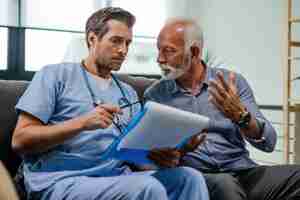 Free photo senior man talking to a doctor who is reading medical test results while being in a home visit