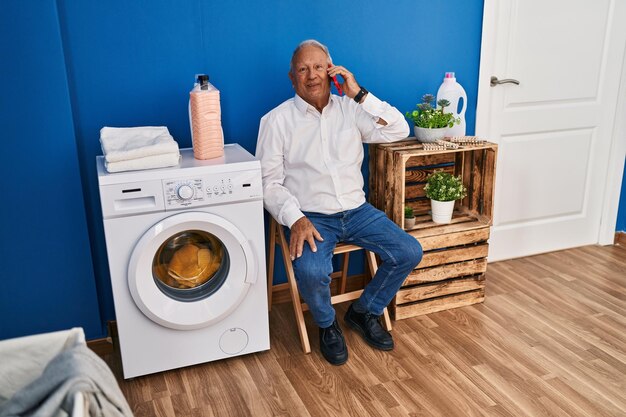 ランドリールームで洗濯機を待ちながらスマホで話すシニア男性