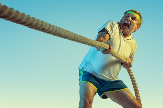 Free photo senior man training with ropes on gradient wall in neon light