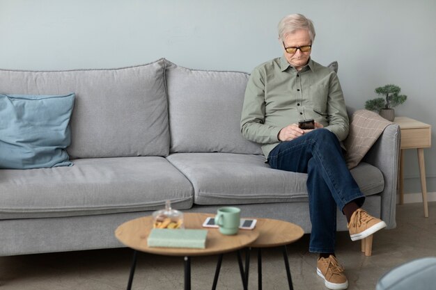 リビングルームのソファに座ってスマートフォンを使用して年配の男性