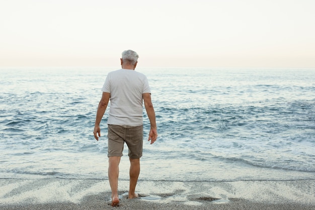 Старший мужчина гуляет в одиночестве на пляже