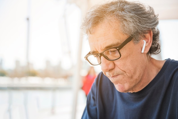Senior man wearing eyeglasses with white bluetooth earphone in his ear