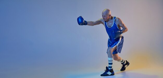 Senior man wearing sportwear boxing isolated on gradient studio wall