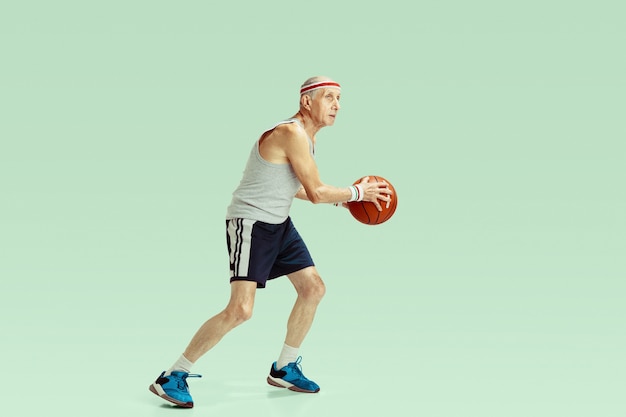 Старший мужчина в спортивной одежде играет в баскетбол на зеленом