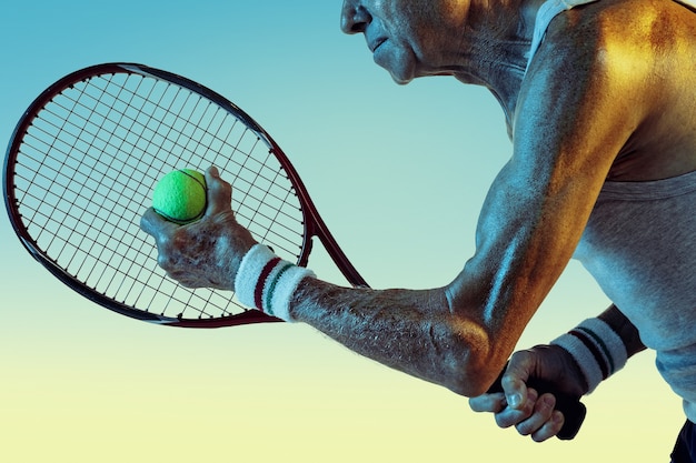 Старший мужчина в спортивной одежде, играя в теннис на градиентном фоне, неоновый свет. Кавказский мужчина-модель в отличной форме остается активным, спортивным. Понятие спорта, активности, движения, благополучия, уверенности.