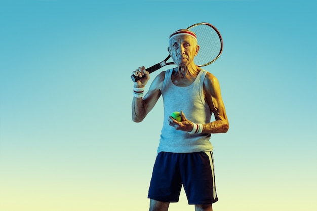 Senior man wearing sportwear playing tennis on gradient