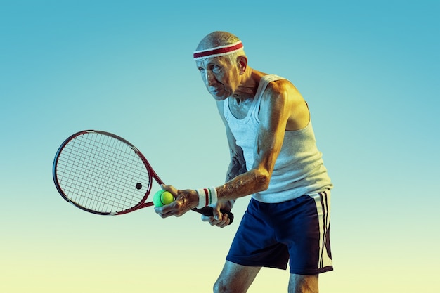Старший мужчина в спортивной одежде играет в теннис на градиенте
