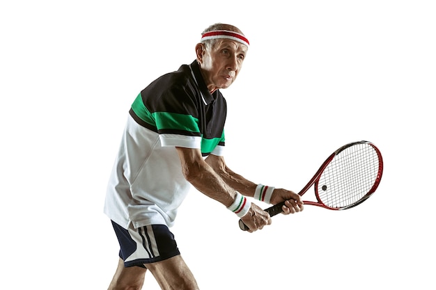 Senior man wearing sportwear playing tennis isolated on white wall. Caucasian male model in great shape stays active and sportive. Concept of sport, activity, movement, wellbeing. Copyspace, ad.