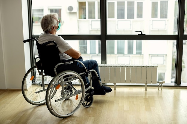 Senior man in wheelchair looking through the window during COVID19 lockdown