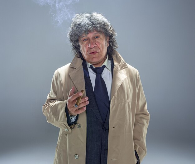 The senior man with cigar as detective or boss of mafia on gray studio space