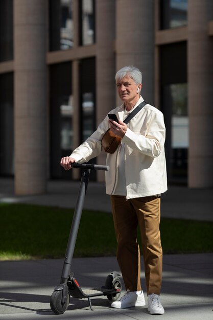 Senior man with an electric scooter in the city using smartphone and earbuds