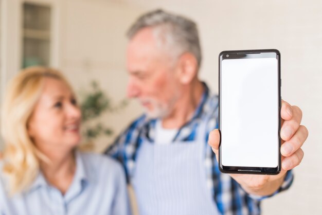Старший мужчина со своей женой, показывая мобильный телефон к камере, держа в руке
