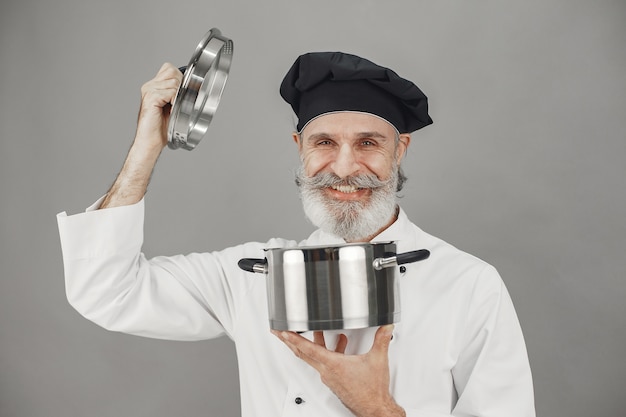 Старший мужчина с металлической сковородой. Повар в черной шляпе. Профессиональный подход к делу.