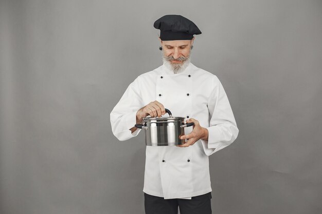 Senior man with metal pan. Chef in a black hat.