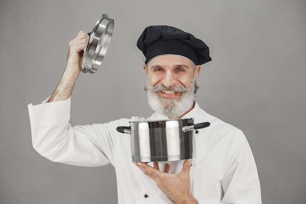 Uomo anziano con padella in metallo. chef con un cappello nero.