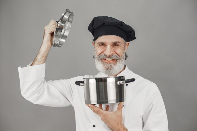 Senior man with metal pan. Chef in a black hat.