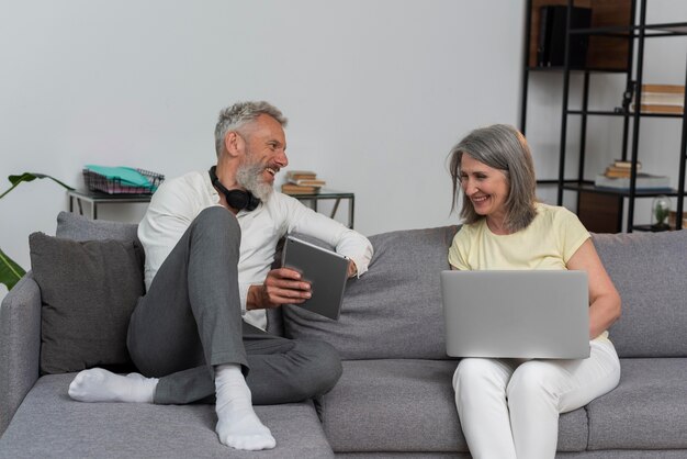 自宅のソファでノートパソコンとタブレットを使用するシニア男性と女性