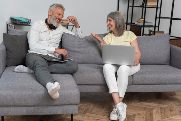 Senior man and woman at home on the couch using laptop and tablet