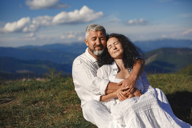 Senior man and woman in the mountains. Adult couple in love at sunset. Man in a white shirt. People sitting on a sky background.