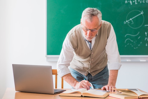 Senior math teacher writing with pen while standing against chalkboard