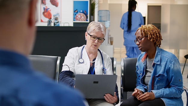 병든 환자에게 노트북으로 진단을 보여주는 수석 의료진은 대기실의 검진 방문 약속에서 질병과 약 치료를 설명합니다. 의사와 건강 검진을 하는 여자.