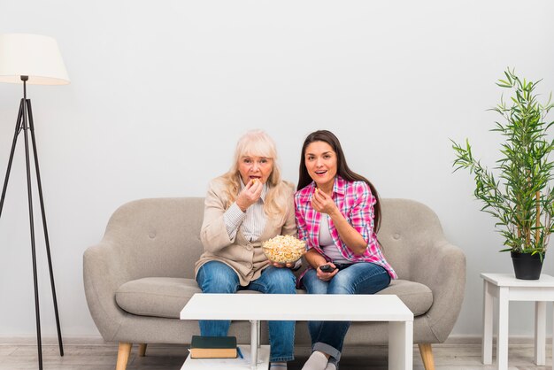 Foto gratuita madre e figlia senior che mangiano i popcorn mentre guardando la televisione a casa