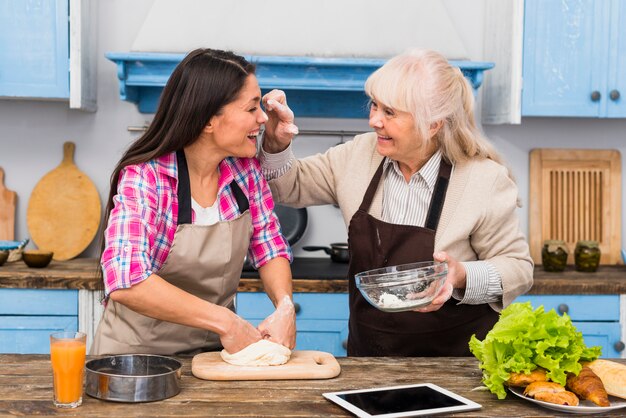 Senior mother and her daughter making fun while kneading the dough