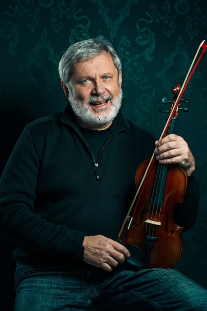 Senior musician playing a violin with a wand on black studio