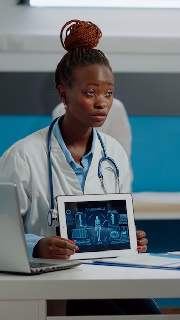 Senior patient and doctor looking at modern tablet with analysis of human body at cabinet desk. Medic having checkup appointment with elder man while using technology in hospital room.