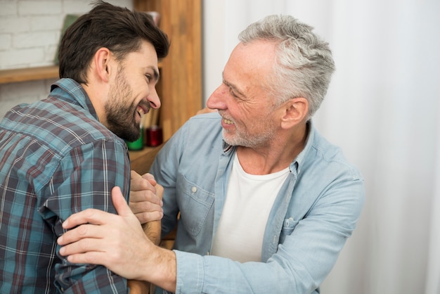 Senior positive man and young happy guy with hands clasped in room