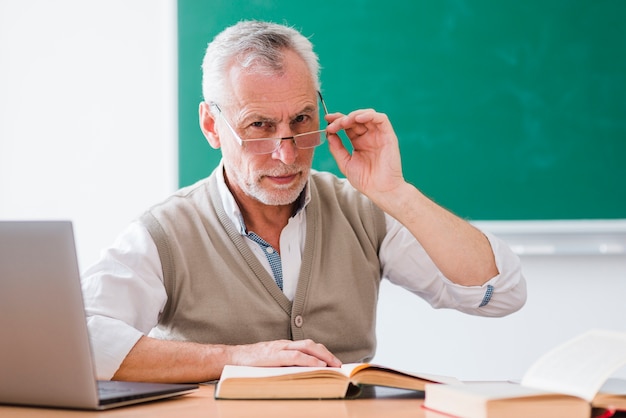 Senior professor correcting glasses and looking at camera in classroom