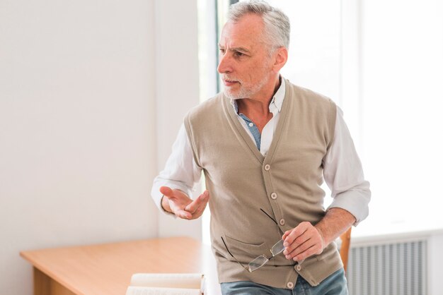 Senior professor explaining lesson near desk in classroom