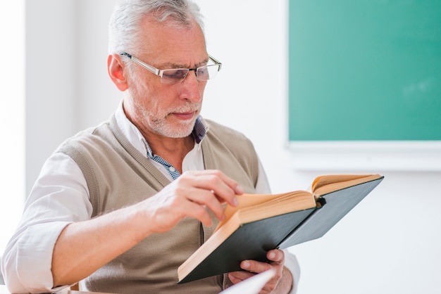 Senior professor reading book while sitting in classroom