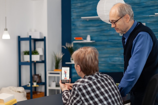 Senior sick man and woman talking with doctor during video call